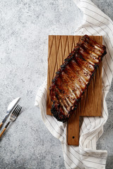 Grilled pork ribs in thick barbeque sauce with sea salt on wooden cutting board with diagonal pattern.  White textured background, white striped towel.