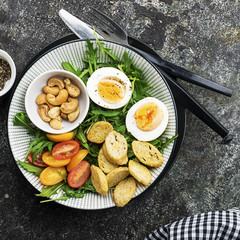 Fresh spring salad with boiled egg, arugula, salad, tomatoes, pecans and crispy toasted bread croutons in a large dish on a gray background. Top view..