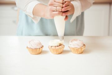 Close up hands of the chef with confectionery bag squeezing cream on cupcakes