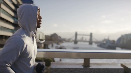 Hooded male jogger running on a bridge in the city, in slow motion