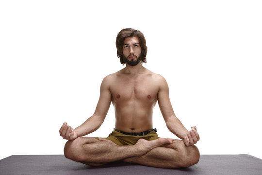 People, rest, relaxation and meditation concept. Isolated portrait of confident advanced young bearded male yoga practitioner exercising on mat, sitting in half lotus posture and making mudra gesture