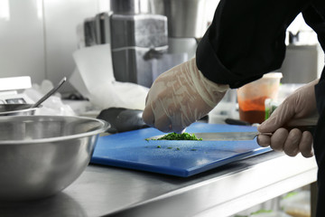 Male chef cutting herbs in restaurant kitchen, closeup