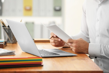 Young man working with laptop and documents in office, closeup