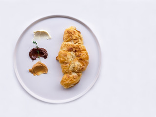 Traditional French breakfast croissant with almonds, chocolate, peanut butter on a white plate, On white table.