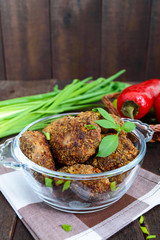 Small meat cutlets in a glass bowl on a dark wooden background.