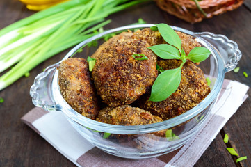 Small meat cutlets in a glass bowl on a dark wooden background.
