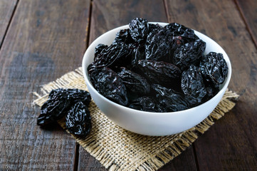 Prunes in a ceramic bowl on a dark wooden background. Dried fruits.