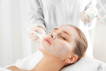 Beautician applying mask onto young woman's face in spa salon