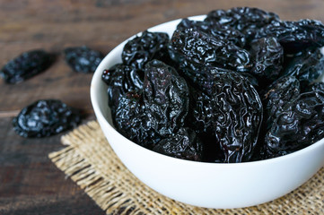Prunes in a ceramic bowl on a dark wooden background. Dried fruits.