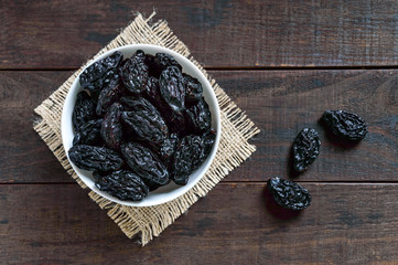 Prunes in a ceramic bowl on a dark wooden background. Dried fruits. The top view
