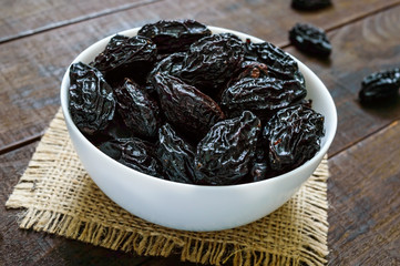 Prunes in a ceramic bowl on a dark wooden background. Dried fruits.