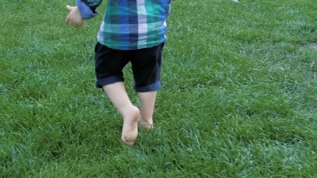 Slow motion closeup footage of adorable toddler boy feet running on fresh green grass at park