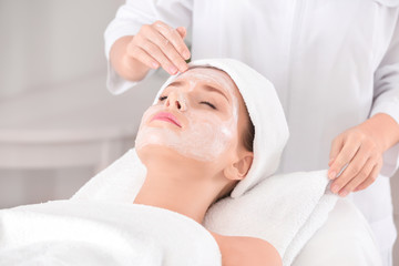 Fototapeta na wymiar Beautician applying cream onto young woman's face in spa salon