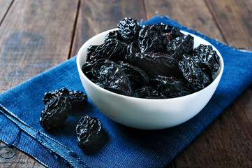 Prunes in a ceramic bowl on a dark wooden background. Dried fruits.