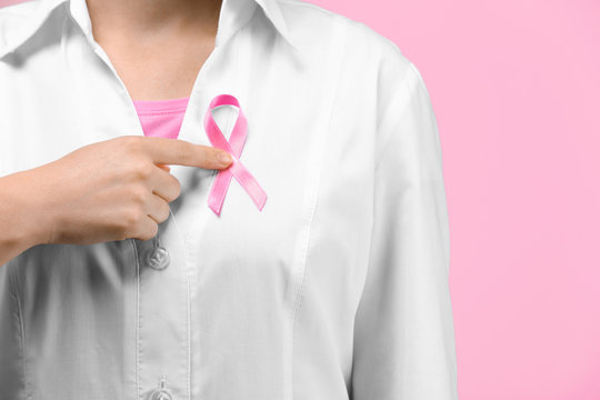 Doctor showing pink ribbon on color background. Breast cancer awareness concept