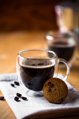 Two cups of espresso coffee on beige napkin in double bottom glasses with butter cookie on wooden brown table background