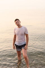Fototapeta na wymiar Young man standing in the water in a wet white t-shirt with protruding nipples