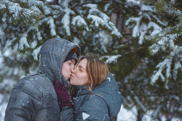 Fototapeta na wymiar Happy snow covered couple kissing under fir branches in winter forest. Concept healthy romantic holidays on fresh air