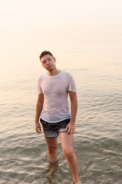 Young man standing in the water in a wet white t-shirt with protruding nipples