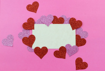 Sparkly pink and red hearts surround a parchment paper tage on a bright pink background for Valentine's Day in February. Copy space