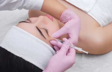 Obraz na płótnie Canvas The doctor cosmetologist makes the Botulinum Toxin injection procedure for tightening and smoothing wrinkles on the face skin of a beautiful, young woman in a beauty salon.Cosmetology skin care.