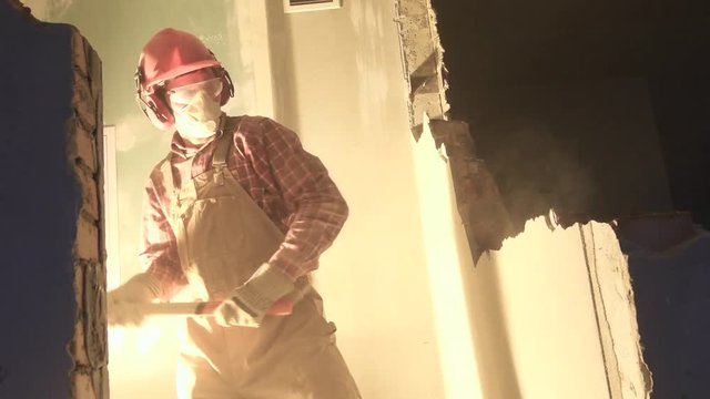 worker with sledgehammer at indoor wall destroying