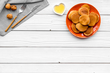 Homemade pancakes on orange plate with toppings honey and nuts. White wooden background top view copyspace