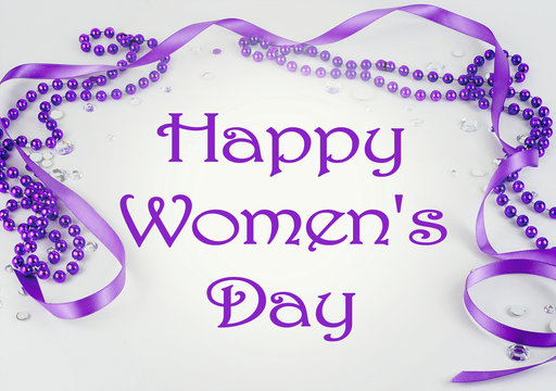 Purple beads and ribbon and sparkly jewels on a light background make a border with message for International Women's Day on March 8th each year.