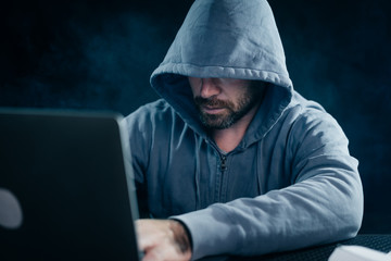mysterious bearded man hides his face under the hood, hacks the laptop