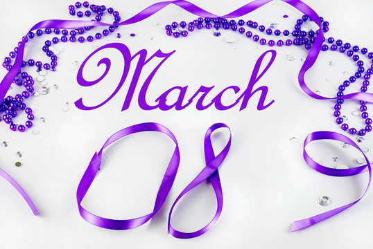 Purple beads and ribbon and sparkly jewels on a light background make a border for International Women's Day on March 8th each year.