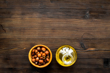 Oil as cosmetics. Haselnut oil near nut in shell on dark wooden background top view copyspace