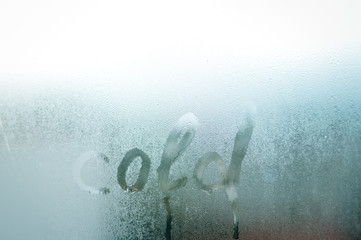 "Cold" word written on fresh condensation on window glass fogged textured background