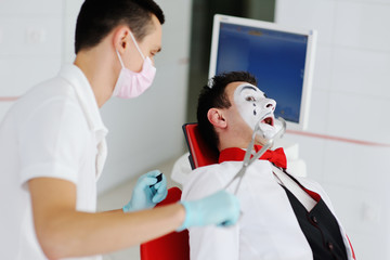 The clown or mime is sitting in the dental chair. The dentist treats the tooth to the patient.