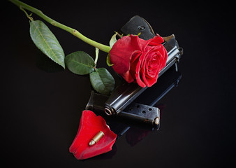 Rose, gun and single bullet on black reflective background