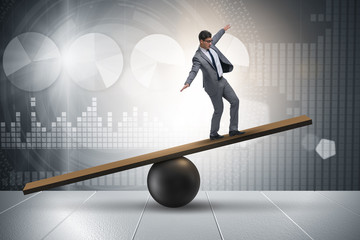 Businessman trying to balance on ball and seesaw