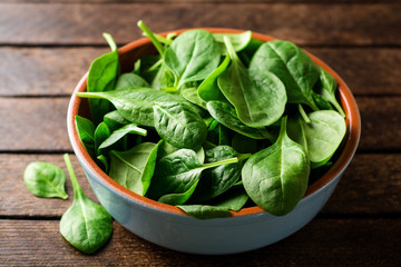 Fresh spinach leaves in bowl on rustic wooden table. Selective focus.