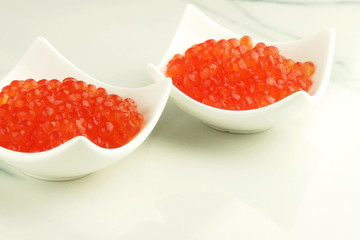 red caviar in white plates on a marble table. copy space