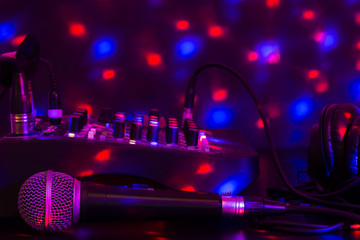 Closeup of microphone, mixing table and headphones with colorful lights.