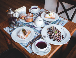 a beautifully served and covered table with different pastries, cinnamon rolls, waffles, a kettle and tea cups