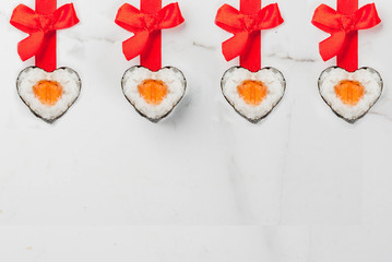 Real sushi set for valentine's day in form of hearts, with red ribbon and bow. White marble background copy space top view