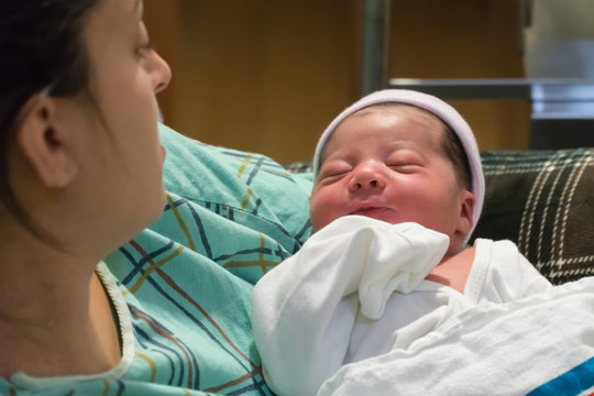 Beautiful newborn baby girl bring held in mothers arms in swaddle blanket after labor and delivery birth in hospital