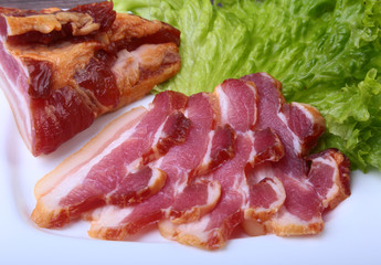 Fresh homemade smoked bacon with leaves lettuce on white plate. Selective focus.