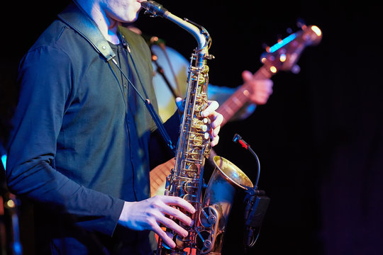 A young guy plays a saxophone with a microphone.