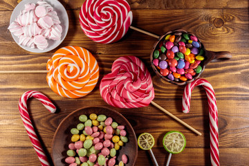 Colorful chocolate candies, lollipops, candy cane and marshmallows on wooden table