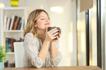 Zelfklevend Fotobehang Woman breathing holding a coffee mug at home © Antonioguillem