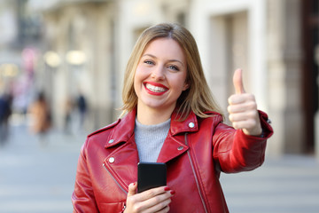 Woman holding smart phone with thumb up on the street
