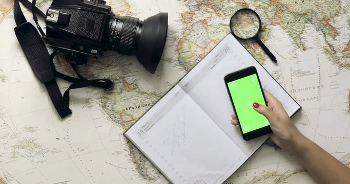 Top view woman traveler hands planning holiday using mobile phone app vintage map from above