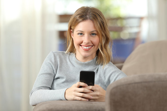 Woman holding a smartphone looking at camera at home