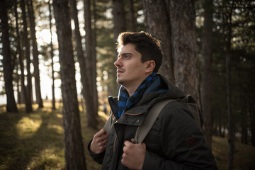 young man in forest holding backpack straps 