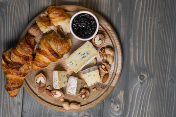 Fototapeta na wymiar Assorted cheese on wooden board plate Camembert or Brie cheese, walnuts, croissant, bread, fruits and berries, dark black wood background, top view.